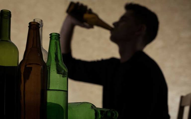 Silhouette of teenage boy drinking from a bottle with bottles in the foreground 