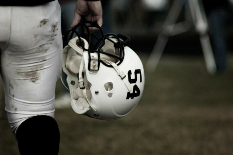 Football player holding a helmet on the sidelines