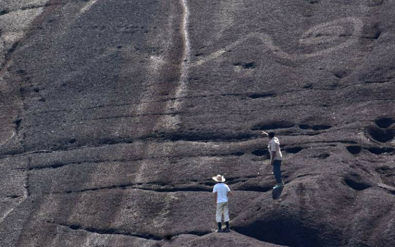 Two researchers inspect the large etchings on the side of a rocky cliff.Two rese