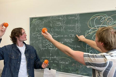 PhD candidates Mick van Vliet and Arno Hoefnagels in front of a chalkboard with,