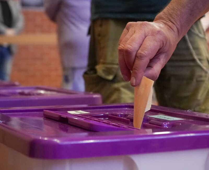 Image of someone's hand dropping their ballot into a voting box