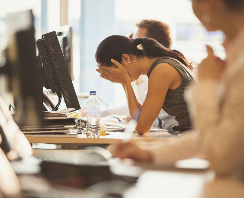 A woman holds her head in her hands at her work desk.