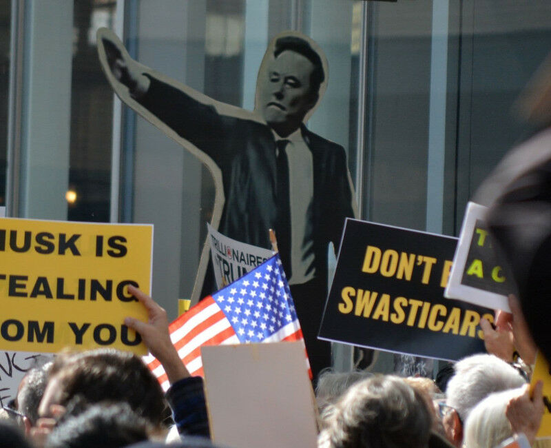 Protest against Elon Musk and DOGE cuts to government funding in front of a Tesl