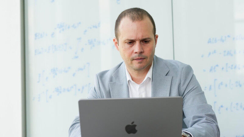 Vlad Gheorghiu works at computer seated in front of a whiteboard with equations