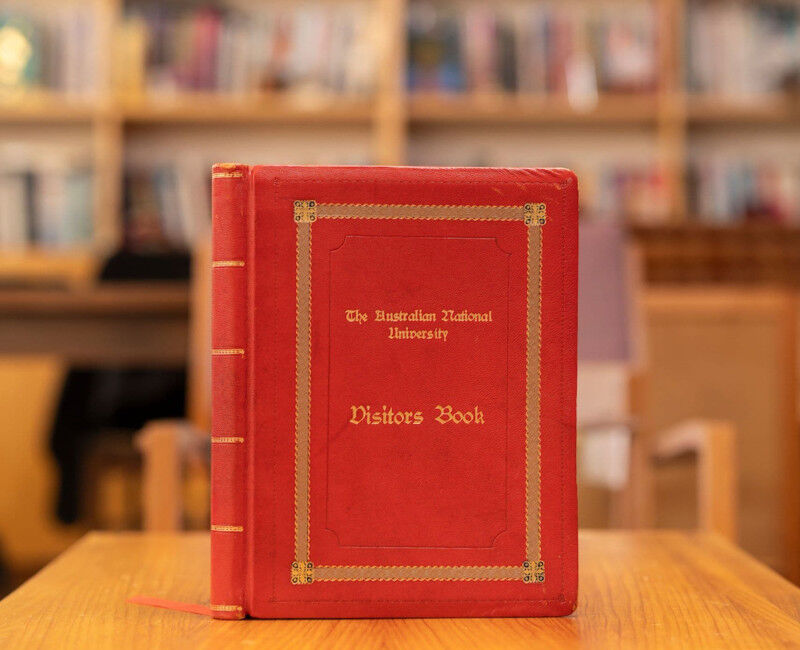 A red leatherbound book with the title 'ANU Visitors Book' stands upri