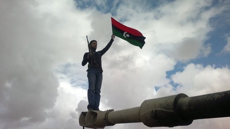 Hussein Elkhafaifi    A rebel waves a Libyan flag while standing atop a tank gun