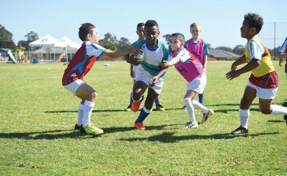 Image credit: NRL - children walking midst game of junior rugby league