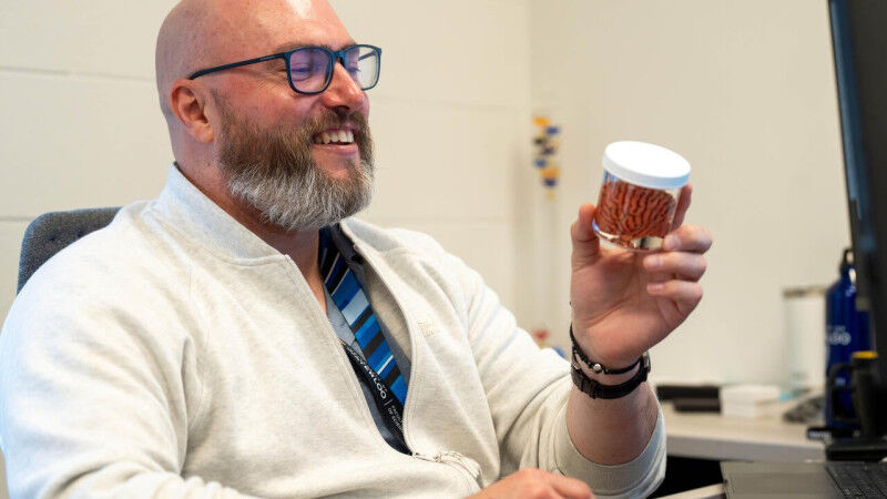 Travis Craddock examines a miniature model of a brain in a jar while seated at h