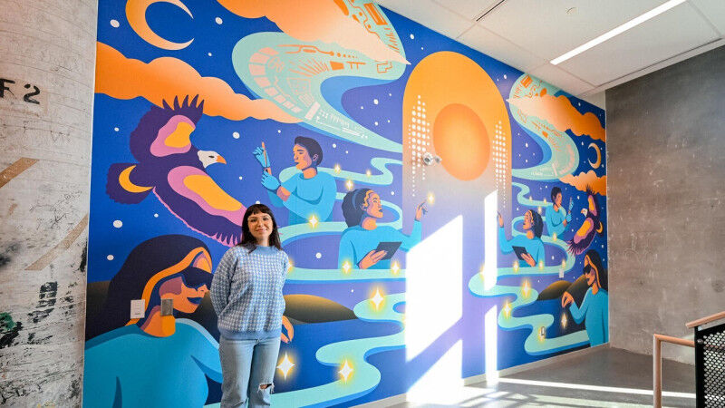 Alanah Jewell standing proudly in front of her Many Hearts, One Mind mural insid