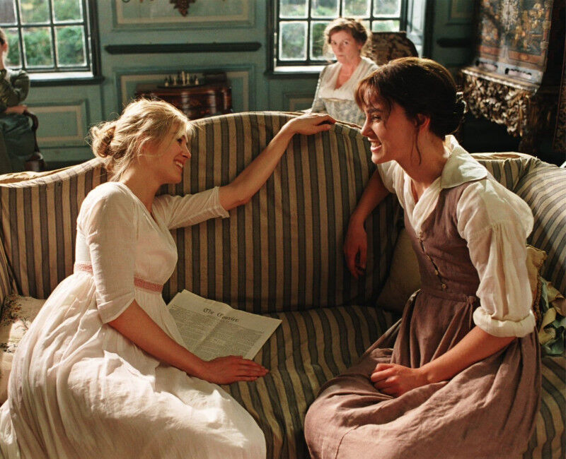 Two women sit on a couch laughing whilst two women sit behind them.